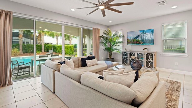 A modern living room with a large sectional sofa, a ceiling fan, and a view of a swimming pool. - Ohana Dream 6 bedrooms, 5 bathroom, private pool, 10 mins from Disney!  (Kissimmee)