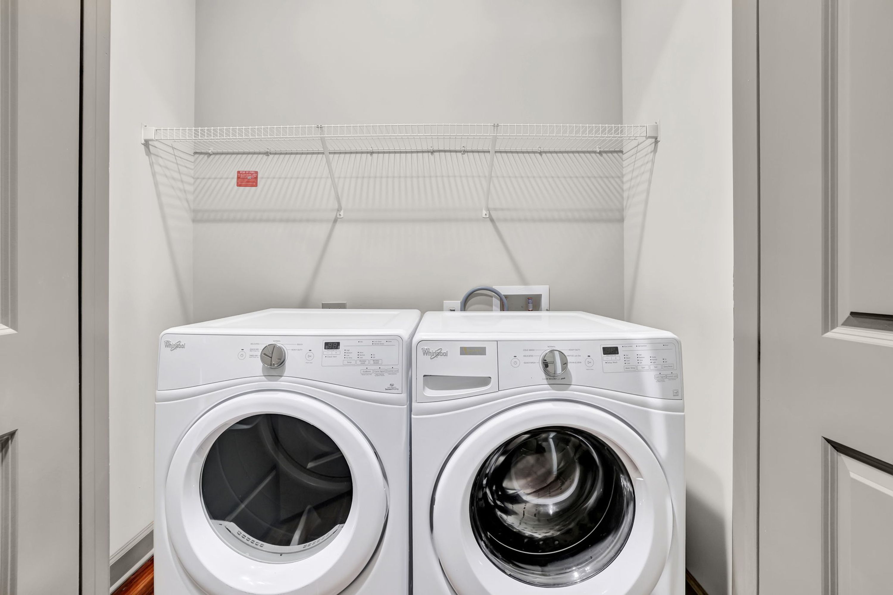 Two white Whirlpool front-loading washing machines in a laundry room with a metal drying rack above.