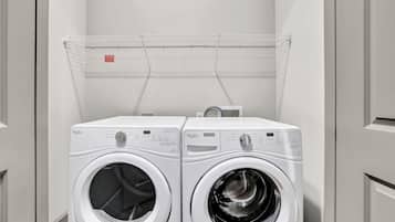 Two white Whirlpool front-loading washing machines in a laundry room with a metal drying rack above.
