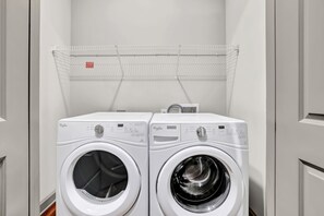 Two white Whirlpool front-loading washing machines in a laundry room with a metal drying rack above. - Ebony Ivory Midtown King Bed (Atlanta)