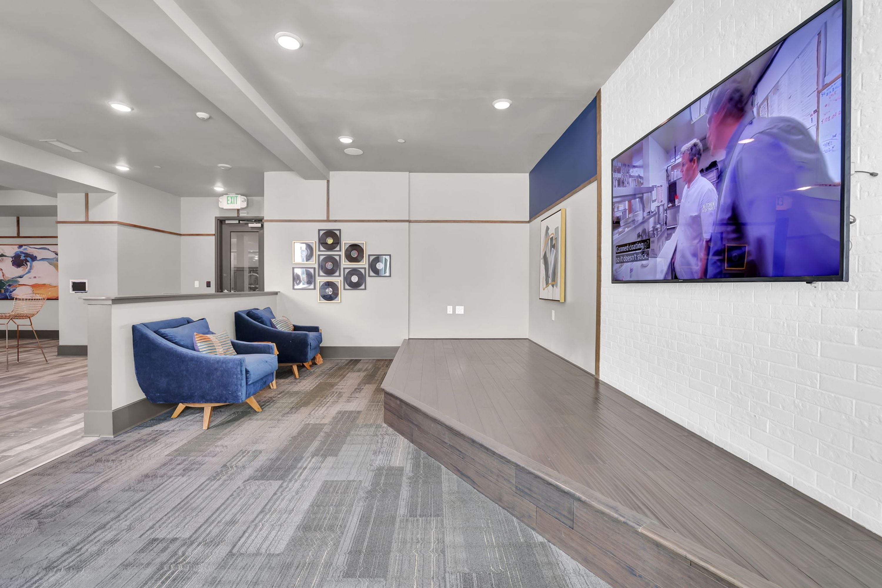Un vestíbulo moderno con mostrador de recepción, asientos azules, un televisor de pantalla plana y una pared con fotografías enmarcadas.