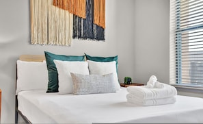 A neatly made bed with white linens and a variety of pillows, including a polka dot one. A small potted plant is on the nightstand beside the bed. - Ebony Ivory Midtown King Bed (Atlanta)
