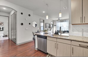 A modern kitchen with wooden cabinets, a dishwasher, and a countertop with a sink. - Ebony Ivory Midtown King Bed (Atlanta)