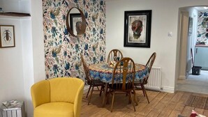 A dining area with a round table and chairs, a yellow armchair, and a colorful cushion on the floor. - North Laine Sunny Cottage with parking (Brighton and Hove)