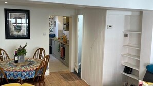 A modern living room with a dining area, wooden flooring, a sofa with colorful cushions, and a kitchen in the background. - North Laine Sunny Cottage with parking (Brighton and Hove)