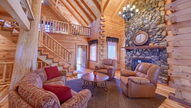 A log cabin interior with a stone fireplace, a wooden staircase, and a cozy seating area. - Treehouse Lodge: Luxury Log Cabin Retreat in Hocking Hills (Laurelville)