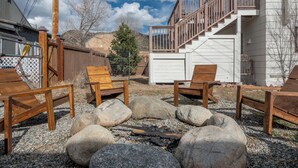 A backyard with a fire pit, wooden chairs, and a staircase leading to a deck.