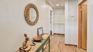 A hallway with a woven mirror, a wooden statue, a framed certificate, and a woven placemat on a green table.