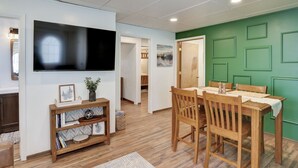 A dining area with a wooden table and chairs, a television mounted on the wall, and a green accent wall.