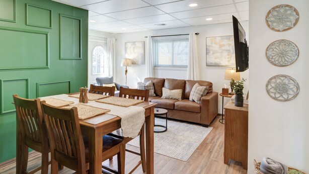 A dining area with a wooden table and chairs, a brown leather sofa, and a TV mounted on the wall.