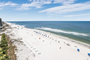 A beach with white sand, a pier, and a building with balconies overlooking the ocean. - Broadmoor 1101 Beach Views From Every Room (Orange Beach)