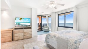 A bedroom with a large bed, a TV, a ceiling fan, and a balcony with a view of the ocean. - Broadmoor 1101 Beach Views From Every Room (Orange Beach)