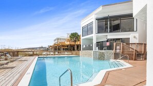 A swimming pool with a wooden deck, a modern building with large windows, and a view of the beach. - Broadmoor 1101 Beach Views From Every Room (Orange Beach)