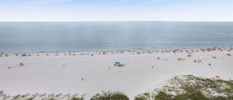 A beach with a wooden walkway leading to a structure, white sand, and a clear sky.