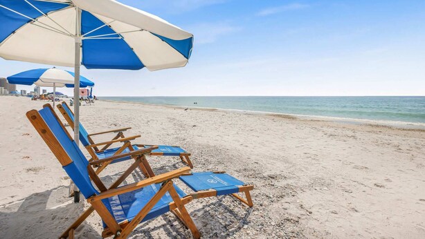 En strand med blå og hvide strandparasoller, træloungestole og krystalklart hav.