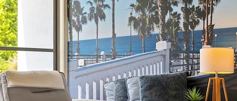 A room with a view of the ocean, a sofa with pillows, a lamp, and a small plant on a side table.