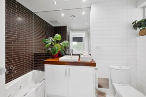 A modern bathroom with a bathtub, a sink, and a toilet. There is a potted plant on the countertop. - Bay View Motel - California Beach (Lorne)