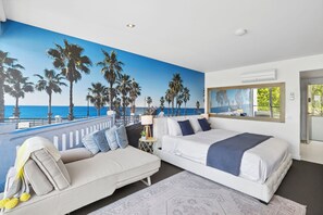 A bedroom with a large beach mural, a bed, a sofa, and a nightstand. - Bay View Motel - California Beach (Lorne)