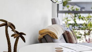 Een kamer met een wandlamp, een houten tafel met een decoratief object, en een raam met uitzicht op groen.
