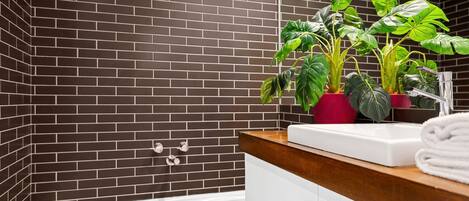 A bathroom with a bathtub, a white sink, and two potted plants.