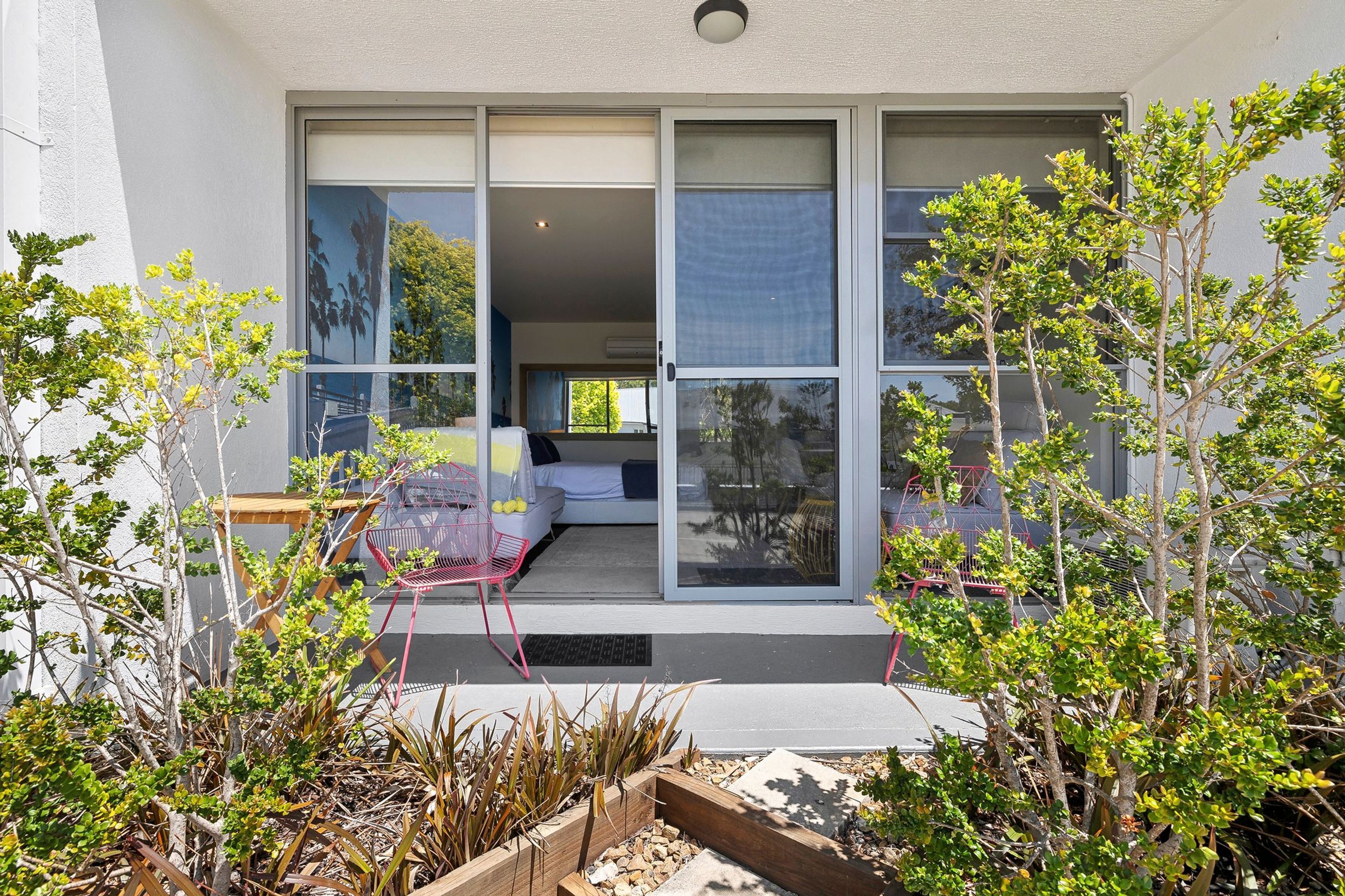 A modern house with large sliding glass doors leading to a bedroom with a bed and a chair.
