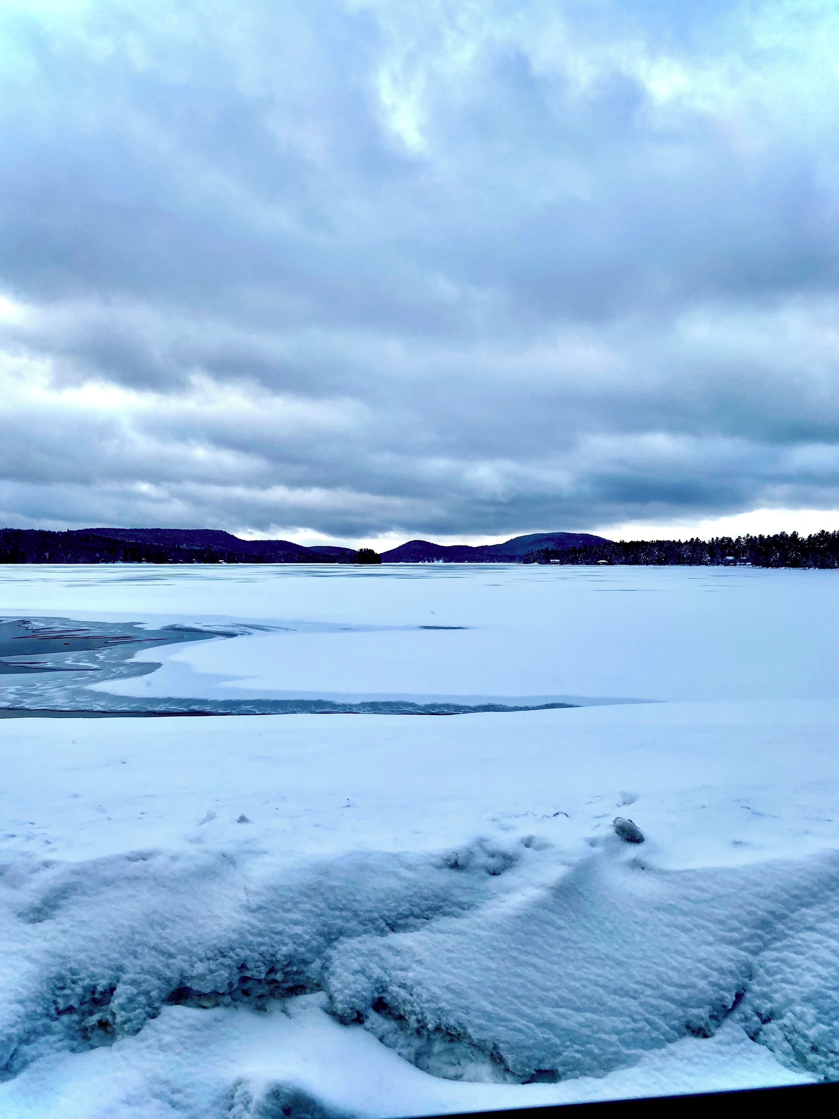 Un paysage hivernal, avec un sol recouvert de neige et des collines qui se dessinent à l’horizon.