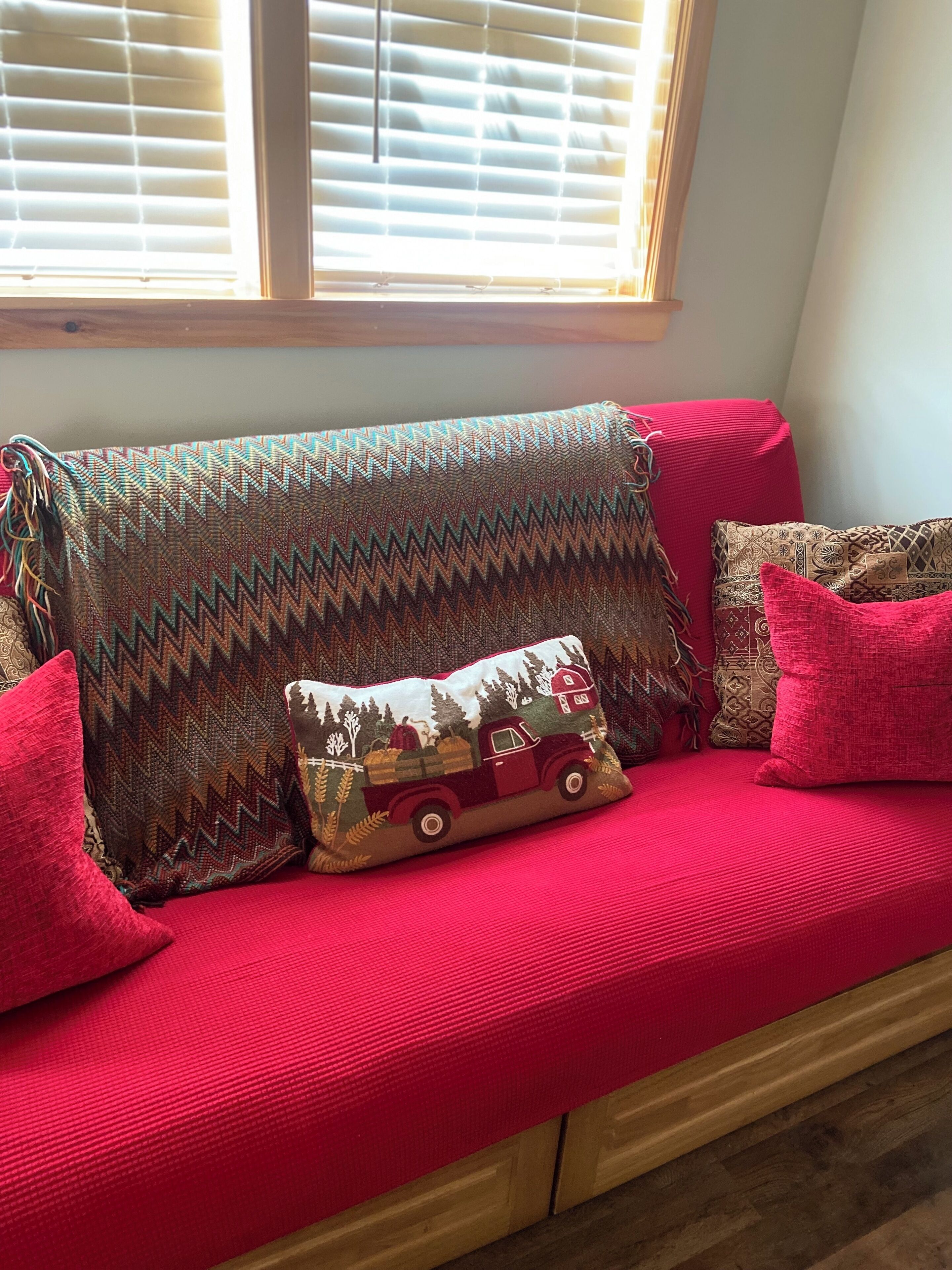 Un canapé rouge agrémenté de coussins à motifs et d’un coussin décoratif orné d’un dessin de camion.