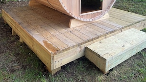 A sauna structure with a wooden exterior, a black roof, and a chimney.