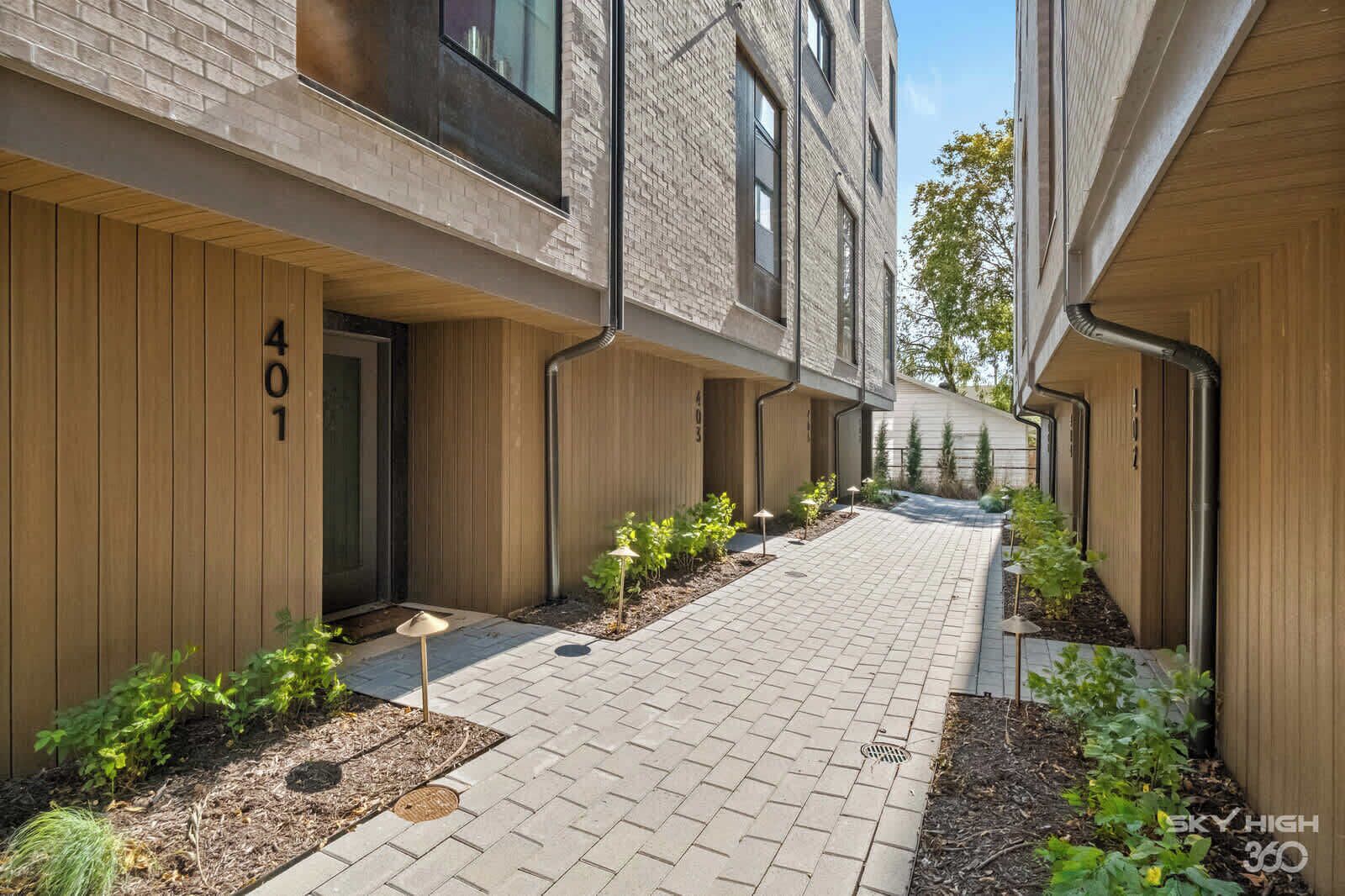 A modern building with a brick facade, numbered 401, and a paved courtyard with small plants and outdoor lighting.