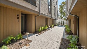 Un bâtiment moderne à la façade en briques, portant le numéro 401, et une cour pavée agrémentée de petites plantes et d’un éclairage extérieur.