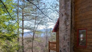 Eine Holzhütte mit Steinaußenwand, einem Balkon und Blick auf Wald und Berge.