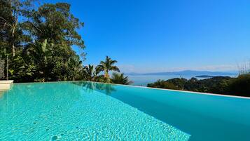Une magnifique piscine à débordement d’un bleu profond, offrant une vue sur l’océan et les montagnes lointaines.