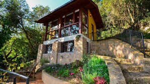 A stone building with a wooden upper level, surrounded by lush greenery and a stone staircase. - Charmosa Suíte em Sambaqui - NDI005 (Florianópolis)