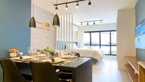 Una habitación de hotel moderna con zona de comedor, cama y ventanas amplias.