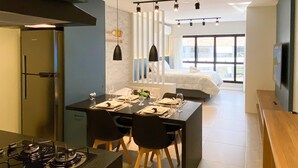 Una cocina moderna con comedor, un ventanal grande y un dormitorio con cama y televisor.