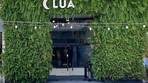 La entrada de un edificio con el nombre 'CLUA' en la parte superior, rodeada de abundante follaje verde.