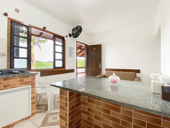A kitchen with a brick backsplash, a gas stove, and a window with multiple panes. - Residencial Verdes Mares (Bombinhas)