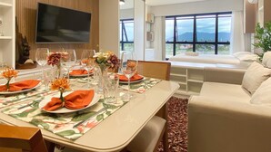 A dining area with a table set for four, a flat-screen TV mounted on the wall, and a large window offering a view of the outdoors.