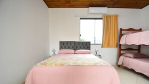 Ein Schlafzimmer mit einem Einzelbett, einem Fenster mit Vorhängen, einer Klimaanlage und einem Etagenbett an der Wand.
