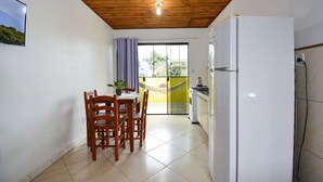 Una cocina compacta con un refrigerador blanco, techo de madera, piso de baldosas y un comedor con mesa y sillas.