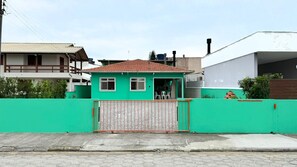 Edificio residencial con fachada verde, techo de tejas y entrada protegida por una reja.