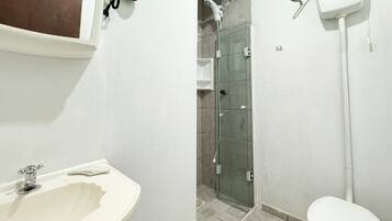 Casa de banho com lavatório branco, cabine de duche em vidro e sanita.