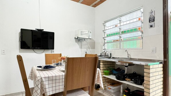A compact kitchen with a dining table, chairs, a TV mounted on the wall, a microwave, and a window with a view of the outside.