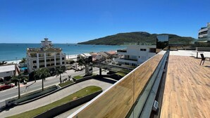 Un edificio moderno con terraza de madera que da a la costa, mostrando vistas al mar y una colina distante.