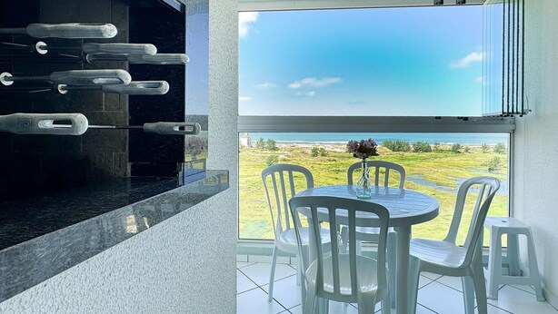 Un balcón con vista a la playa, una parrilla y una mesa con sillas.
