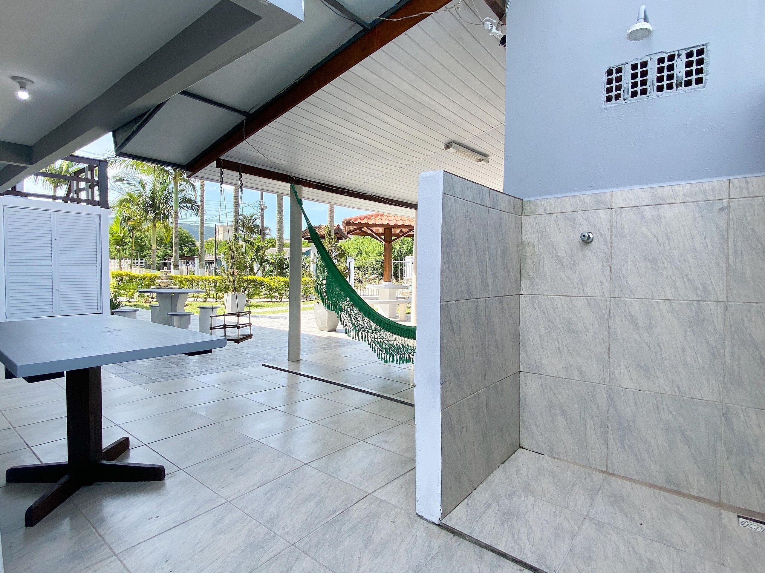 Uma área externa moderna com mesa, cadeiras, rede e chuveiro.