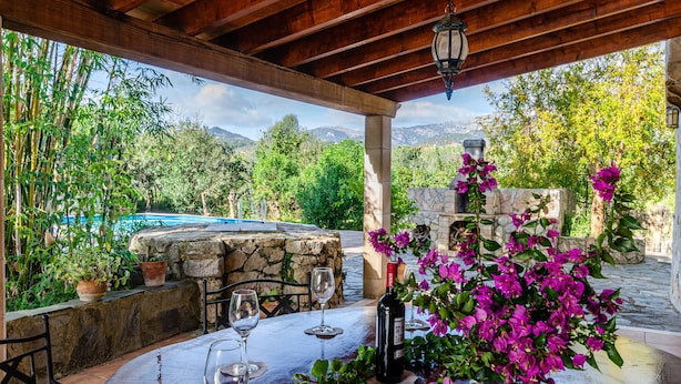 An outdoor patio with a stone table, wine glasses, and a bottle of wine.