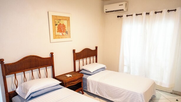 A hotel room with two single beds, a wooden nightstand, a framed picture on the wall, and an air conditioning unit. - Charming 2-bedroom condo, with WiFi, AC & uninterrupted sea views in Bridgetown  (Bridgetown)