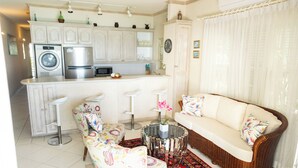 A modern kitchen with white cabinets, a built-in washing machine, and a microwave. There is a wicker sofa with cushions and a patterned rug. - Charming 2-bedroom condo, with WiFi, AC & uninterrupted sea views in Bridgetown  (Bridgetown)