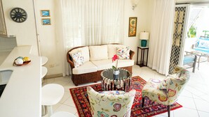 A living room with a sofa, chairs, a coffee table, and a dining area with a table and chairs. - Charming 2-bedroom condo, with WiFi, AC & uninterrupted sea views in Bridgetown  (Bridgetown)